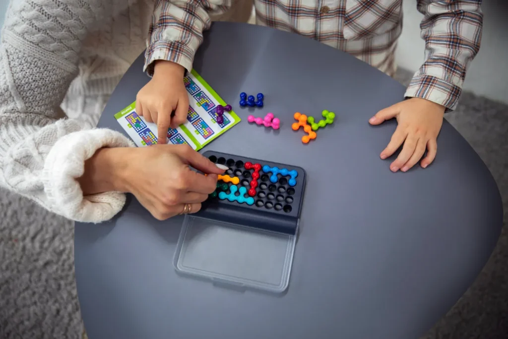 Criança montando quebra-cabeça educativo com peças coloridas sobre uma mesa azul, enquanto encaixa os encaixes no tabuleiro e organiza as formas no brinquedo.