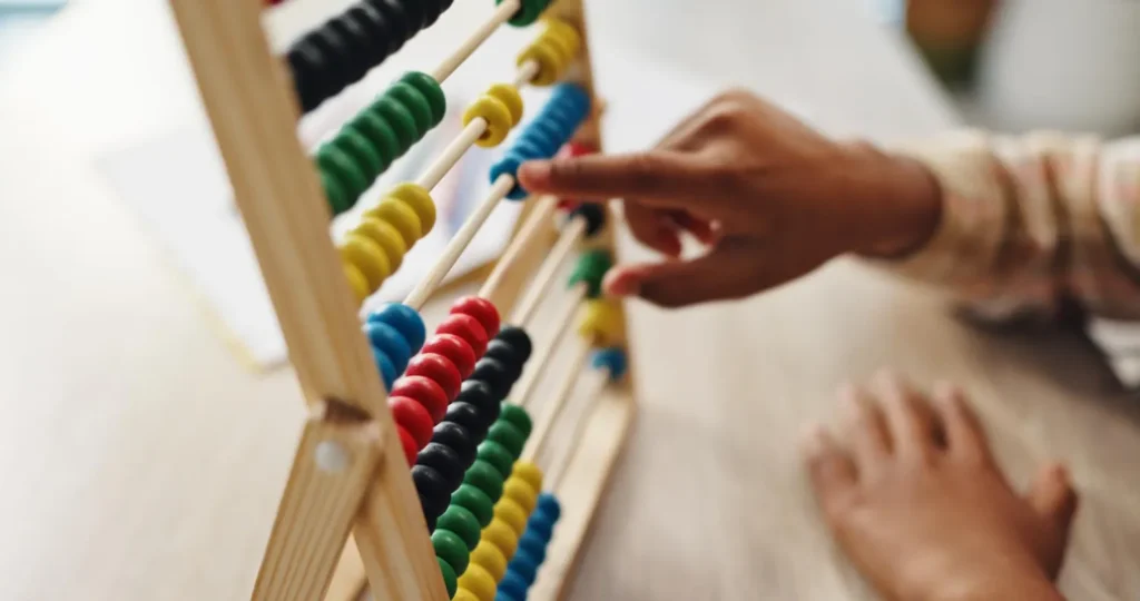 Mão de uma criança brincando com um ábaco de madeira com contas coloridas, em ambiente doméstico, com foco nos arcos e nas cores do instrumento.