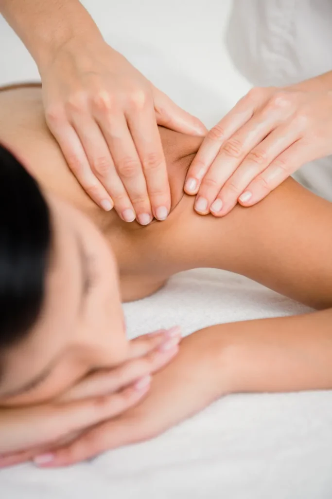 Mãos fazendo massagem relaxante nas costas de uma pessoa, pressionando suavemente o músculo em ambiente de spa, com foco na terapia manual