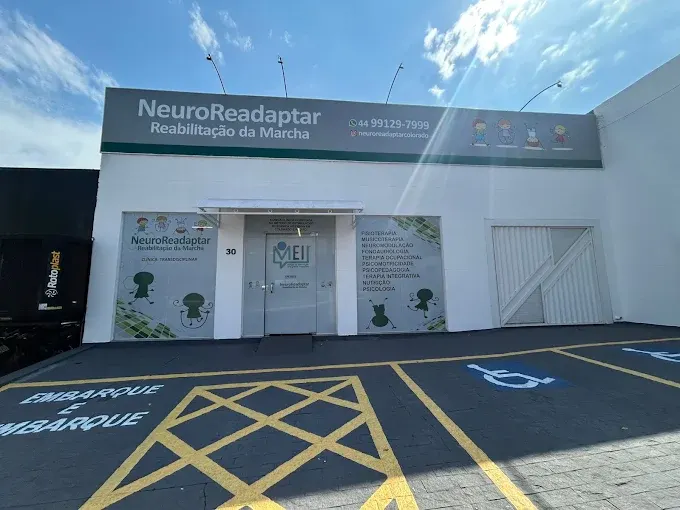 Fachada de uma clínica chamada NeuroReadaptar Reabilitação da Marcha, com banner e porta de entrada, na frente de uma área externa com marcações no chão para acessibilidade.